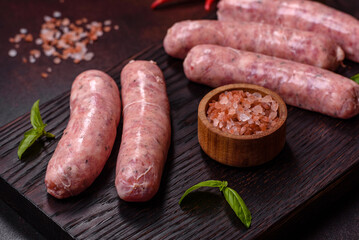 Raw sausages with ingredients on a cutting board on a dark concrete background with copy space