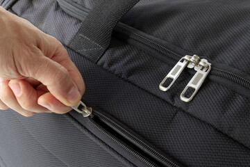 hand opening the zipper of a black travel bag, close up © OLEKSANDR