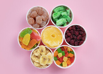 Dried fruits in round containers. Background with a mix of healthy snacks. Assorted vitamin food on a pink background.