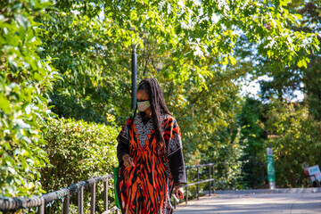 an African American woman with long braids wearing an orange and black tiger striped dress carrying...
