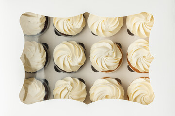 Set of brown chocolate and white vanilla cupcakes with whipped cream cheese tops in the white gift box. Flat lay