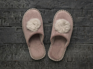 Pink homemade women's slippers on a wooden background. The concept of home shoes.