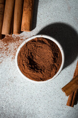 Ceylon cinnamon sticks and ground cinnamon bowl. Carelessly scattered cinnamon on the background. Top view.