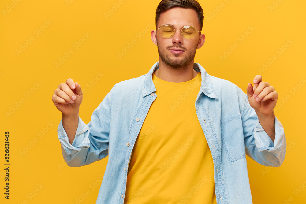 Wall mural Joyful dancing happy tanned handsome man in blue shirt sunglasses enjoy cool mood posing isolated on orange yellow studio background. Copy space Banner Mockup. Holiday concept