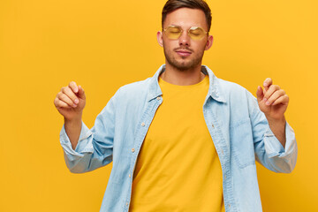 Joyful dancing happy tanned handsome man in blue shirt sunglasses enjoy cool mood posing isolated on orange yellow studio background. Copy space Banner Mockup. Holiday concept