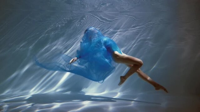 Attractive young woman swims beautifully underwater in a blue dress dress. slow motion