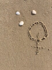 In the sand on the beach is carved the sign for female