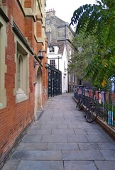 A alley in Cambridge. A narrow street, a red brick tenement house on the left. On the right side, bicycles are parked by the railing