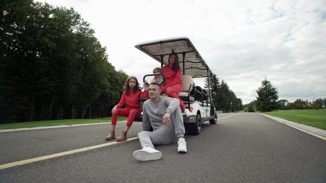 Parents and children pose for a photo next to a golf cart in the park. Happy family together on vacation. Smiles of a boy and a girl. High quality 4k footage