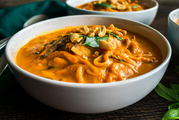 Spicy Thai Curry Pumpkin Noodle Soup Garnished with Peanuts and Thai Basil: Thick soup or stew made with pumpkin, rice noodles, and shiitake mushrooms
