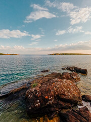 Spectacular Sunset Views of Lake Superior from the Coast of Isle Royale National Park. Lichen covered rocks are in the forefront of view. Small islands covered in green evergreen trees in the distance