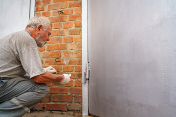 an elderly gray-haired man paints the metal garage door with a roller. 