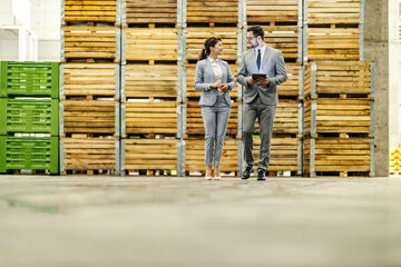 Full length of businesspeople walking around warehouse and monitoring on tablet.
