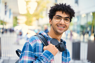 Egyptian student wearing headphones smiling to the camera while standing with backpack. Education...