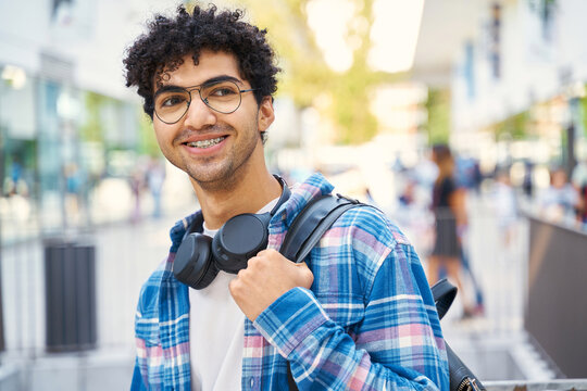 Middle eastern man smiling looking away with backpack standing on the street 