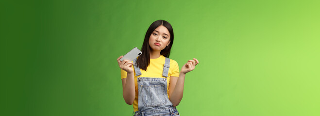 Bored indifferent cool urban asian girl waste time summer holiday alone, playing smartphone game, interrupt texting, browsing internet, gesturing reluctant, look sad, losing battle, green background - obrazy, fototapety, plakaty