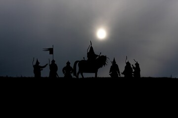 Silhouettes of medieval knights on a horse carrying a flag on dramatic scene