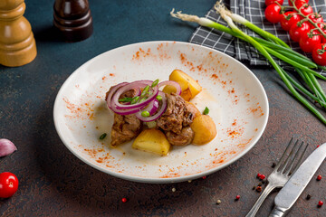 Kazan kebab on plate with beef, potato and red onion on dark table