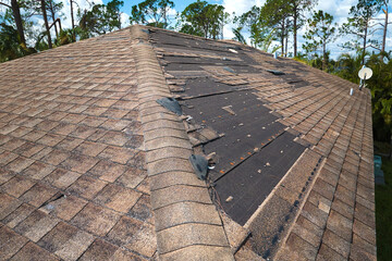 Damaged house roof with missing shingles after hurricane Ian in Florida. Consequences of natural...