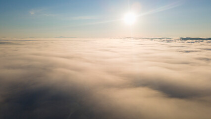 Fototapeta na wymiar Sky, Sunrays, Sunrise and Horizon over a clouds cover mountains ridge and pipe plant, aerial
