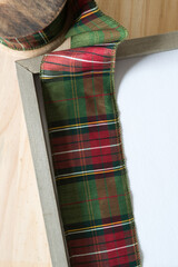 spool of holiday fabric ribbon in green and red plaid and white panel framed in wood
