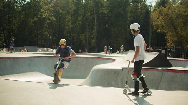 Man making trick on kick scooter in concrete bowl, air extreme in skate park, grab and barspin jump, young skater boy. 