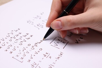 Student writing different mathematical formulas on paper, closeup