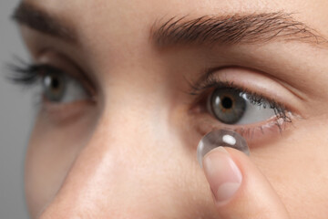 Woman putting in contact lens on grey background, closeup view