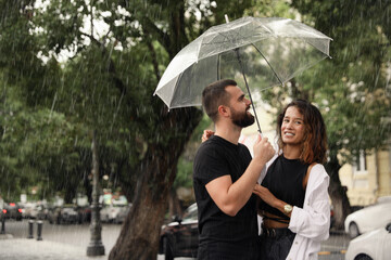 Young couple with umbrella enjoying time together under rain on city street, space for text