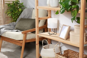 Obraz na płótnie Canvas Wooden shelving unit with home decor, folding screen and armchair near light wall in room. Interior design