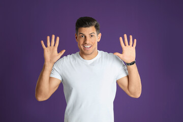 Fototapeta premium Man showing number ten with his hands on purple background