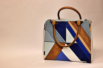 Beautiful women's handbag in blue, white, brown, light blue colors on a light background.