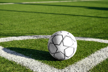 A white and black soccer ball in the corner of the field on the artificial green grass of the stadium with markings