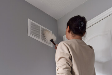 Woman cleaning return air vent with duster
