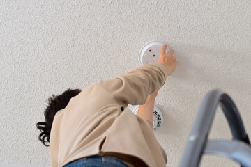 Woman reaching up for smoke alarm on ceiling at home