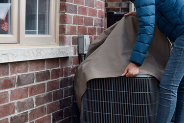 Woman putting cover on air conditioner unit outside the house
