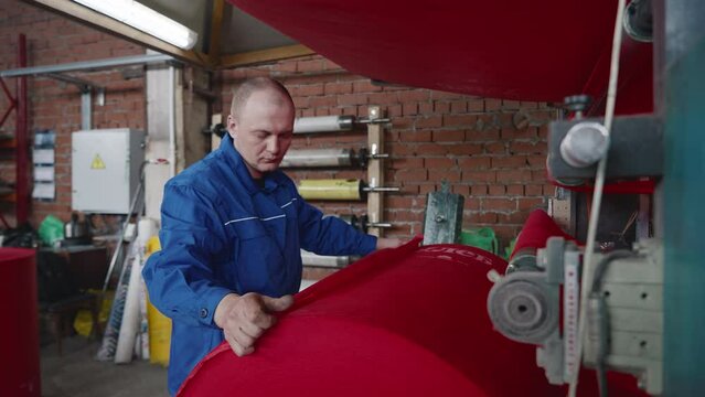 An engineer threads the ecological fabric material into the production equipment. An engineer puts the red fabric material into the processing machine. An engineer inserts fabric material into machine