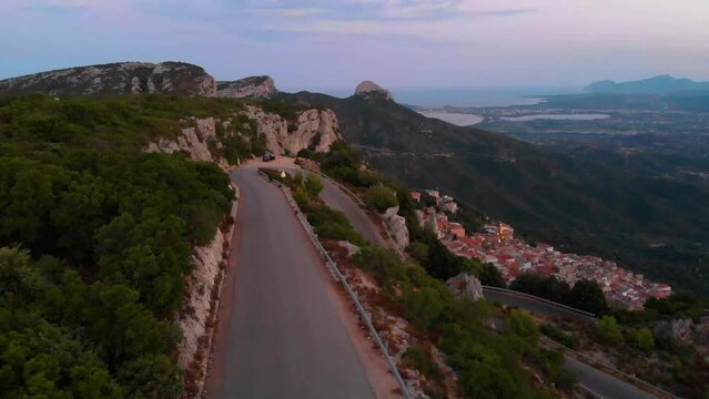 Sinkflug mit Drohne auf der Insel Sardinien in Italien am Meer in Europa der K&uuml;ste entlang &uuml;ber eine Berg Stra&szlig;e Bergpass mit Blick auf die Stadt Baunei und mediterraner Landschaft in der D&auml;mmerung 4k