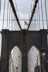 Cables leading up to a Brooklyn Bridge suspension tower, with an American flag on top