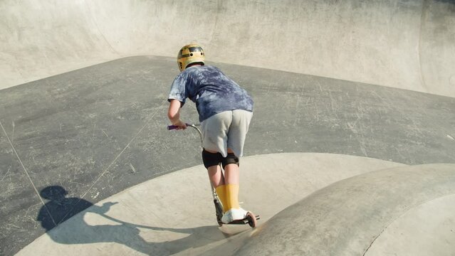 Man making trick on kick scooter in concrete bowl, air extreme in skate park, grab and barspin jump, young skater boy. 