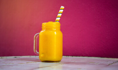 Mango smoothee with straw on a wooden table on pink background