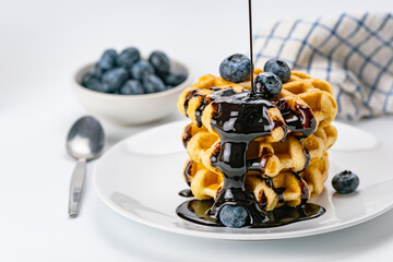 Pouring chocolate syrup on stack of fresh delicious homemade waffles topping with ripe organic...