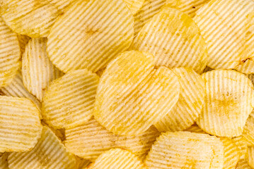 Top view of salted dry crispy fried corrugated potato chips. Crispy potato chips delicious appetizer snack on the floor.