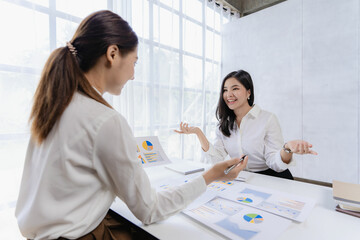 Fototapeta premium Two Asian businesswomen attending two Asian business partners discuss the financial and company planning graph during a budget meeting.