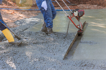 Using tamping machine, compacted layer fresh concrete is aligned on new driveway construction.