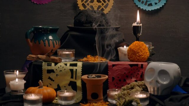 Traditional mexican bread of the dead "pan de muerto" with black ashes in Mexican altar with &ldquo;papel picado&rdquo;, copal, incense burner, cempasuchil flowers, coffee, pumpkin, ceramic skull. Slow motion. 