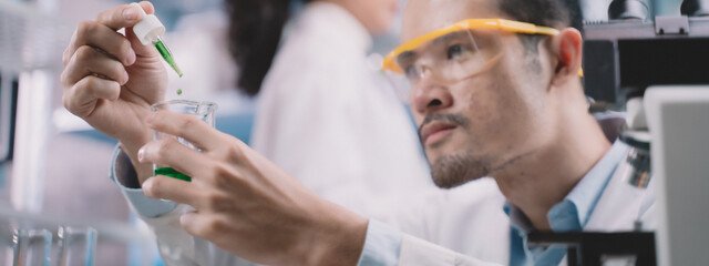 Researcher man are drop liquid to a beaker in his hand and researcher woman are picking up the...