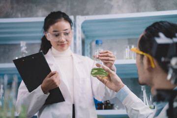 A standing female researcher handing a sample of liquid in tube to a researcher sitting in the laboratory.