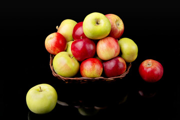 Ripe red and green apples in a wicker vase autumn harvest on a black background.