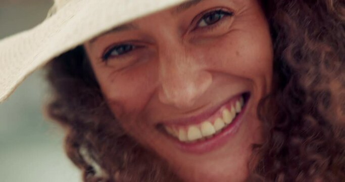 Happy, woman and macro view of a face with a smile laughing in the wind enjoying summer. Portrait of a person feeling happiness, freedom living and vacation fun with a sun hat on a windy day